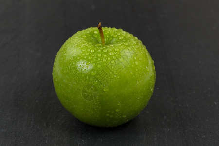紧贴着一整块新鲜的绿苹果上面覆盖着水滴下面有天然石块选择地聚焦于水果的前部图片