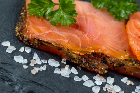 精细切片的熏鲑鱼倾斜角度在天然石块上有粗咸盐选择地集中在鲑鱼的前面部分图片