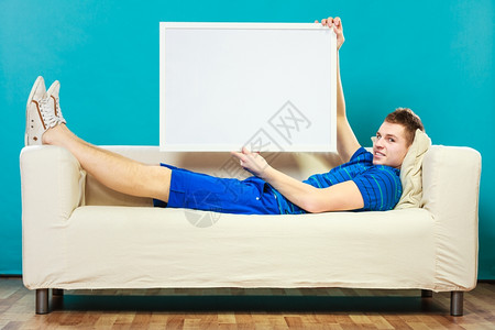 广告概念年轻人躺在沙发上用空白的演示文稿板男模型显示标志广告牌复制蓝色文本的空间图片