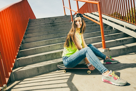 酷的长发少女坐在城市楼梯附近的滑板上活跃生方式在夏天很怪异图片