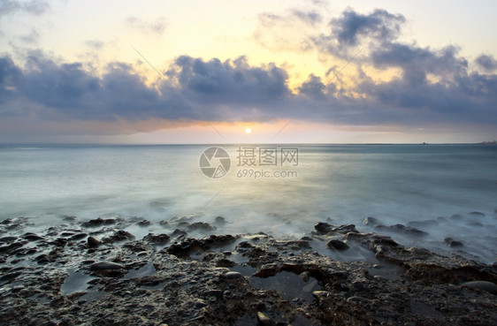 在岩石海滩美丽的日落水在运动中模糊不清图片