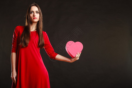 爱和感情穿红衣的年轻美女拿着心箱送礼物在工作室的灰色背景上图片