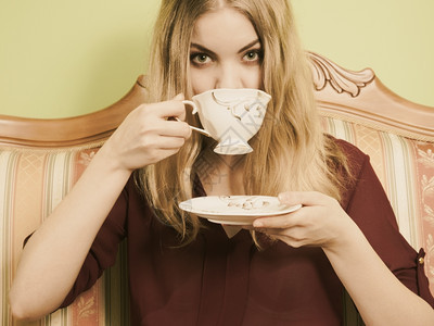 时装女人坐在古老沙发上喝咖啡着热汽水的年轻女孩保持清醒咖啡因能量塞皮亚图片