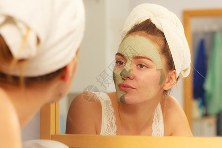 女在浴室除去面部粘土泥罩女在镜子前洗手间除去面部干土泥罩在镜子前洗手间除去海绵皮肤护理女孩照顾她的外衣美容疗养所院图片