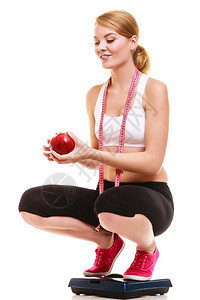 享受快乐的年轻女孩带着体重比的测量胶带将苹果孤立在白色背景上健康生活方式的概念图片