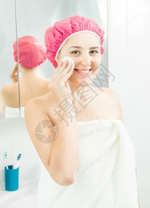 洗完澡后用面霜擦脸的美丽微笑着的女人肖像图片