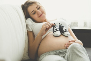 身躺在沙发上并穿着婴儿靴子的幸福孕妇照片图片