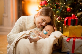快乐的年轻母亲在圣诞树下与新生儿子一起装扮图片