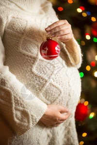 穿着羊毛服装在圣诞树上摆布的孕妇近身照片图片