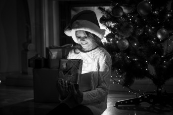 黑色和白照片可爱笑女孩的微看着里面圣诞夜的发光礼物盒图片