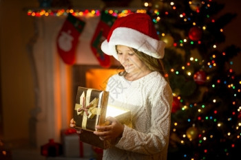 穿着圣塔帽的快乐女孩拿着发光的礼物盒图片