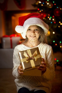 可爱笑女孩的肖像假扮成壁炉和圣诞树的礼物盒图片