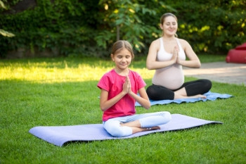 年轻孕妇和可爱女孩在公园草地上做瑜伽图片