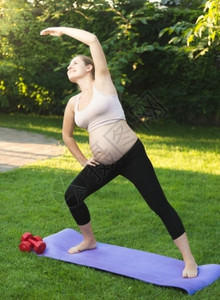 美丽的孕妇在公园绿草地上运动图片