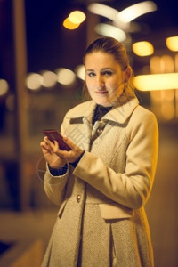 在街上使用手机的优雅年轻女子夜装肖像图片