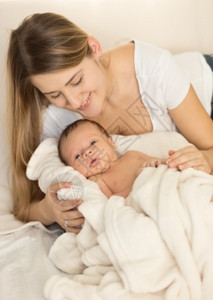 年轻有爱心的母亲抱在床上新生婴儿的画像图片