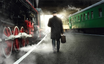 身戴保龄球帽的人后视镜和在平台上行走的手提箱在蒸汽机车旁边图片