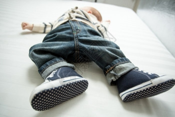 穿着牛仔裤和穿着运动鞋躺在床上的男婴脚图片