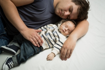 年轻父亲与新生儿男孩在床上睡觉的肖像图片
