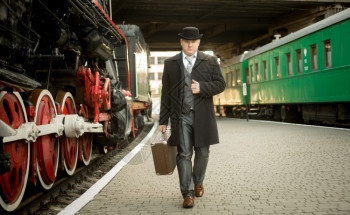 穿旧西装的帅男穿着手提箱在火车平台上行走图片