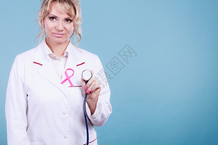 医生有粉色癌症带乳腺医疗帮助治概念穿白色围裙的金发女医生穿着粉色丝带蓝背景的听诊器图片