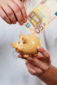 男人用钞票和小猪银行的手花钱概念男人用小猪银行和欧元钞票现金的手储蓄金融高清图片素材
