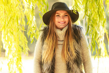 可爱的美女穿着黑色帽子毛皮腰衣的围着公园柳树的叶子图片