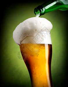以绿色背景将啤酒倒入玻璃杯图片