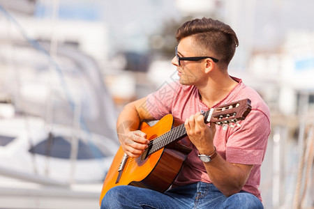 年轻人弹吉他浪漫音乐声男化的概念年轻人弹吉他男孩坐在码头玩乐器图片