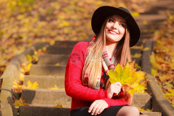 秋天公园的美丽女子秋天公园的迷人笑年轻女子拿着大金叶的肖像穿着红毛巾和黑帽子的时装女孩图片