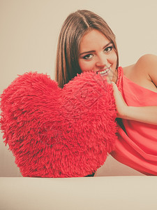 在白沙发上坐着带红色的心形枕头微笑着可爱的年轻女孩情人节的爱图片