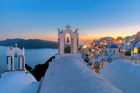 依拉苏火山口希腊圣托里尼岛Oia或Ia日落时的Oia或Ia有钟白房子和教堂的拱门白房子和教堂有蓝色圆丘背景