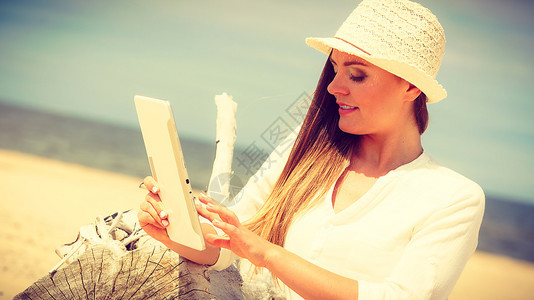 海边有石板的女孩技术娱乐长发的美人沙滩上带平板电子书的草帽美人暑假在新鲜空气中休息的女学生图片
