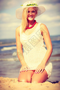 迷人的女士坐在沙子上夏天人们的观念漂亮白裙子和帽图片