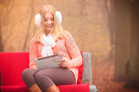 美丽的女士有数字平板电脑秋天外面的人年轻女士坐在长椅上穿着秋天服图片