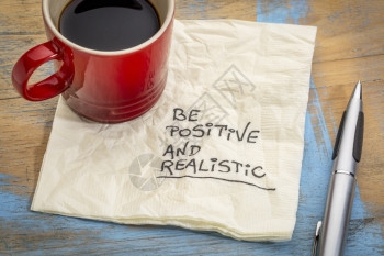 积极和现实笔迹在餐巾纸上加一杯咖啡图片