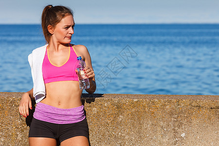 穿运动服的妇女休息从塑料瓶中补充饮用水休息后在海边户外运动锻炼后休息图片