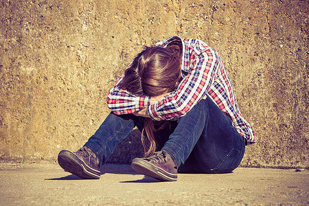 一个人独自坐在户外的墙壁上头部被肩膀遮盖失业抑郁或悲伤的概念图片