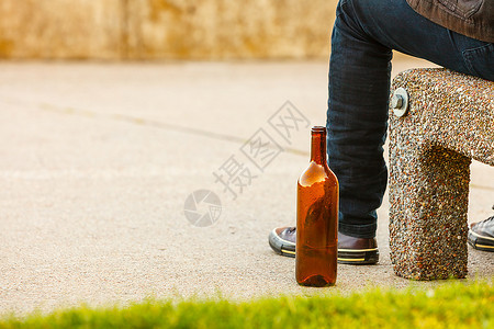 一个人在户外的长椅上被酒瓶压抑。 一个人在户外的长凳上被酒瓶压抑。 人们和酗酒问题。图片