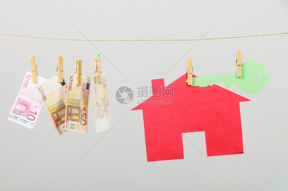 红房子绿色钥匙和钞票现金挂在灰色背景的洗衣线上出售和购买家庭概念图片