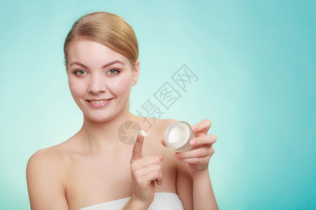 美容治疗女在脸上涂润湿奶油持有皮肤护理产品的罐子绿蓝背景摄影棚拍图片