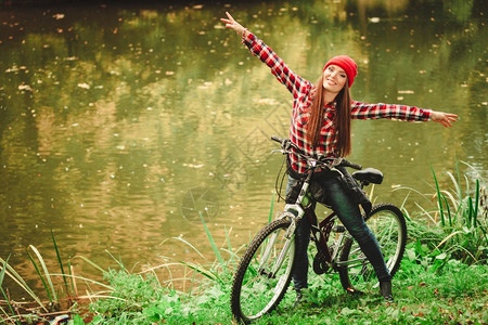 年轻女子骑着自行车在公园水潭边比划手势图片