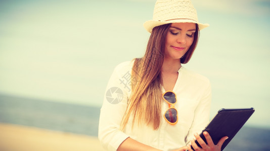 海边有石板的女孩技术娱乐长发的美人沙滩上带平板电子书的草帽美人暑假在新鲜空气中休息的女学生图片