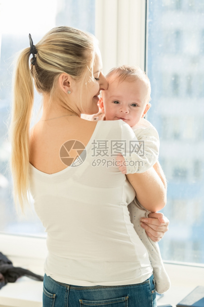 美丽的母亲肖像拥抱着她三个月大的婴儿男孩在窗边图片