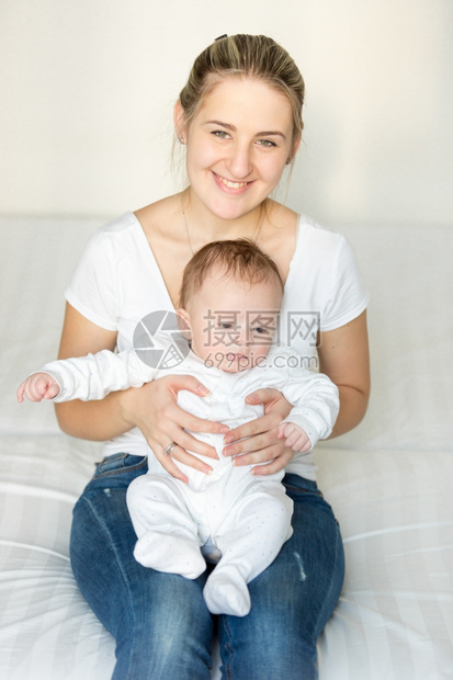 年轻微笑的母亲肖像坐在她三个月大的婴儿旁边图片