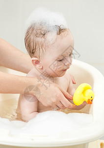 与黄橡皮鸭在泡沫浴中玩耍的可爱小男孩肖像图片