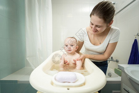年轻笑的母亲在浴室塑料池洗她可爱的婴儿图片