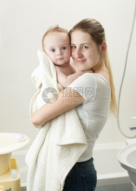 快乐的年轻母亲洗澡后抱着婴儿的肖像图片
