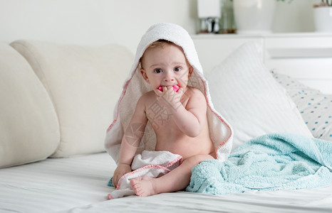 九个月大的婴儿男孩坐在毛巾下面的床上图片