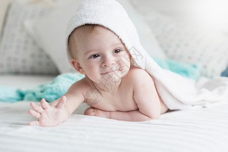 快乐9个月大的婴儿躺在床上白毛巾下图片